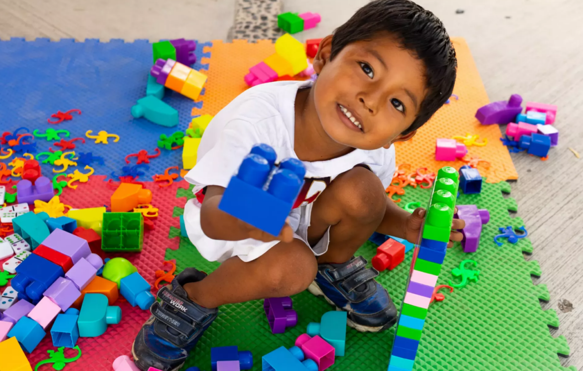 Niño comparte su opinión mientras un adulto lo escucha con atención en la escuela.
